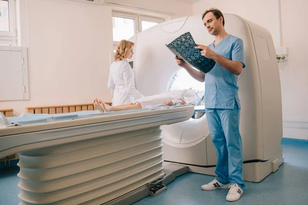 Attentive doctor looking at tomography diagnosis while radiologist operating ct scanner during patients diagnostics — Stock Photo