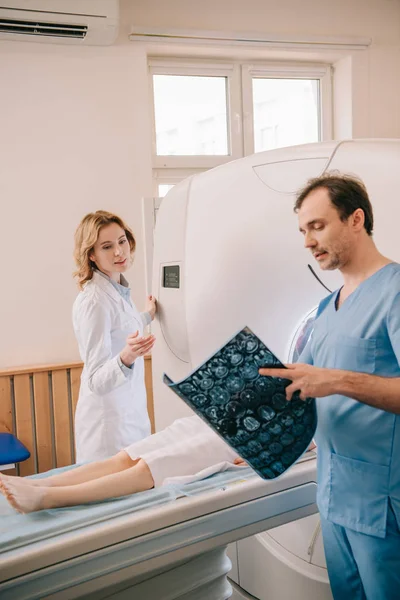 Arzt schaut sich Tomographie-Diagnose an, während Radiologe CT-Scanner während der Patientendiagnose bedient — Stockfoto