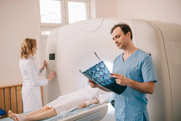 Médico atento olhando para o diagnóstico de tomografia enquanto o radiologista operando tomógrafo durante o diagnóstico dos pacientes — Fotografia de Stock