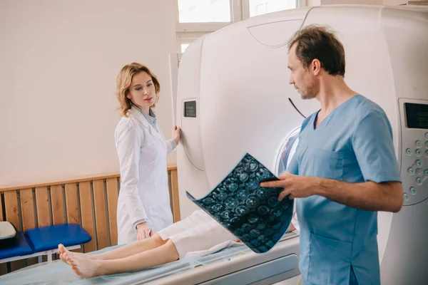 Doctor holding tomography diagnosis while radiologist operating ct scanner during patients diagnostics — Stock Photo