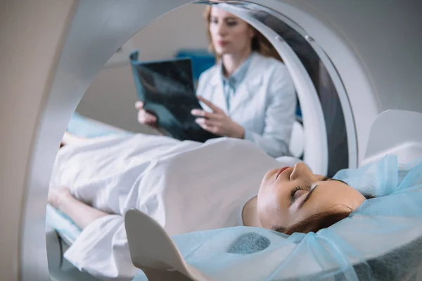 Foco seletivo do radiologista segurando o diagnóstico de raios-x enquanto o paciente deitado no leito do tomógrafo durante o diagnóstico — Fotografia de Stock