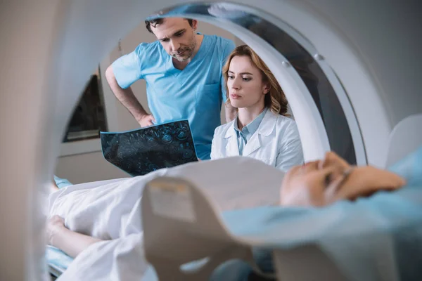 Selective focus of thoughtful doctors looking at x-ray diagnosis during patients diagnostics on ct scanner — Stock Photo