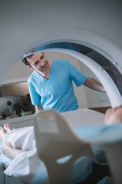 Selective focus of smiling radiologist looking at patient during diagnostics on computed tomography scanner — Stock Photo