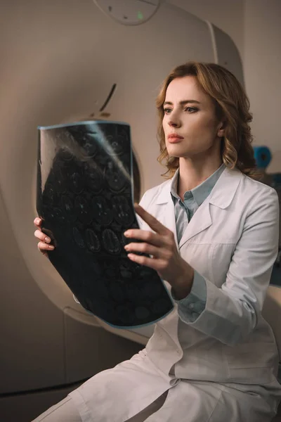 Radiologista atento examinando o diagnóstico de raios-x enquanto sentado perto do tomógrafo computadorizado — Fotografia de Stock