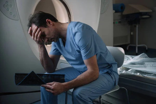 Exhausted sitting near computed tomography scanner in hospital and holding x-ray diagnosis — Stock Photo