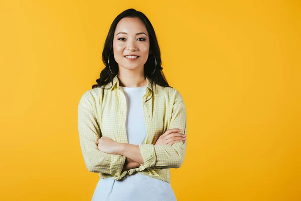 Smiling asian girl with crossed arms isolated on yellow — Stock Photo