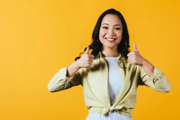 Smiling asian woman showing thumbs up isolated on yellow — Stock Photo