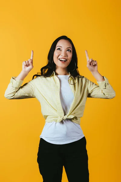 Schöne lächelnde asiatische Mädchen zeigt nach oben isoliert auf gelb — Stockfoto