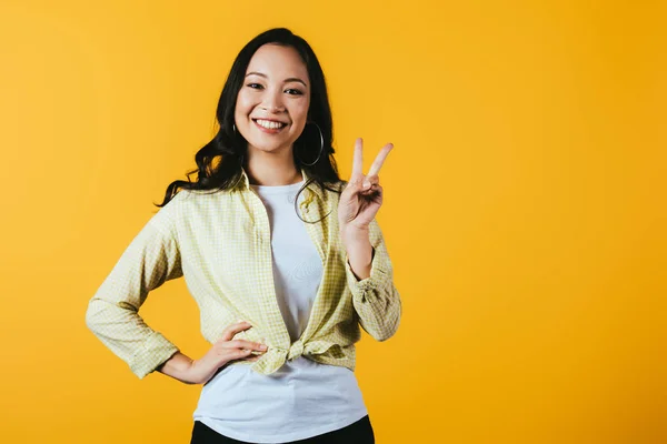 Красива азіатська дівчина показує знак перемоги ізольовано на жовтому — стокове фото