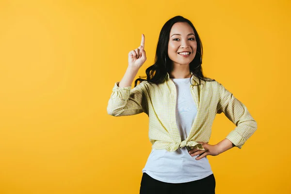 Attraktive glücklich asiatische Mädchen zeigt nach oben isoliert auf gelb — Stockfoto