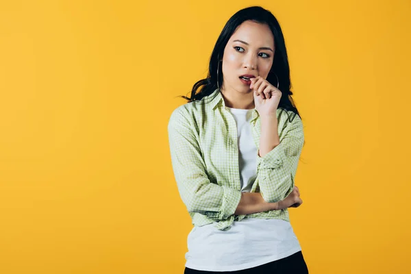 Attractive brunette asian girl thinking isolated on yellow — Stock Photo