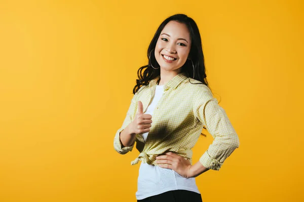 Cheerful asian girl showing thumb up isolated on yellow — Stock Photo