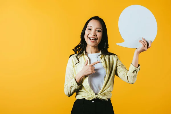 Mujer asiática casual apuntando a la burbuja del habla, aislado en amarillo - foto de stock