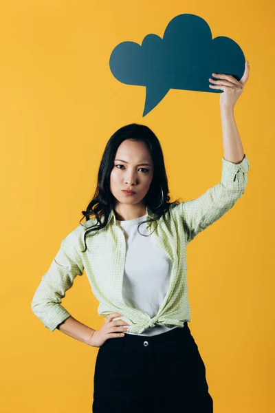 Mujer asiática disgustada sosteniendo la burbuja del habla, aislado en amarillo - foto de stock