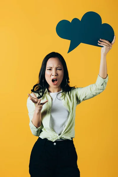 Irritado asiático mulher gritando e segurando nuvem discurso bolha, isolado no amarelo — Fotografia de Stock