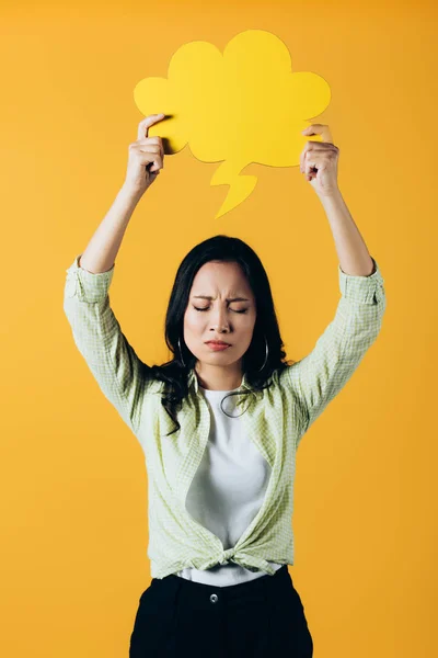 Роздратована азіатська дівчина тримає хмарну бульбашку мовлення, ізольована на жовтому — стокове фото