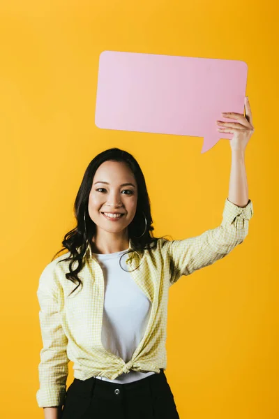 Atractiva mujer asiática sosteniendo la burbuja del habla rosa, aislado en amarillo - foto de stock