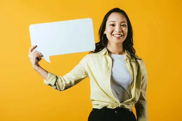 Sorridente asiatico ragazza holding discorso bolla, isolato su giallo — Foto stock