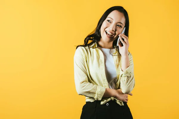 Brunette asian girl talking on smartphone isolated on yellow — Stock Photo