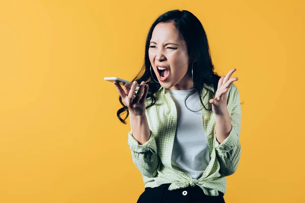 Agresivo asiático chica gritando en smartphone aislado en amarillo — Stock Photo