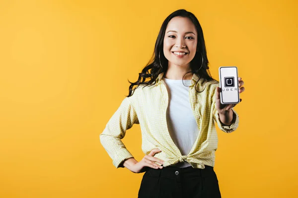 KYIV, UKRAINE - 16 de abril de 2019: menina asiática sorridente mostrando smartphone com aplicativo uber, isolado em amarelo — Fotografia de Stock