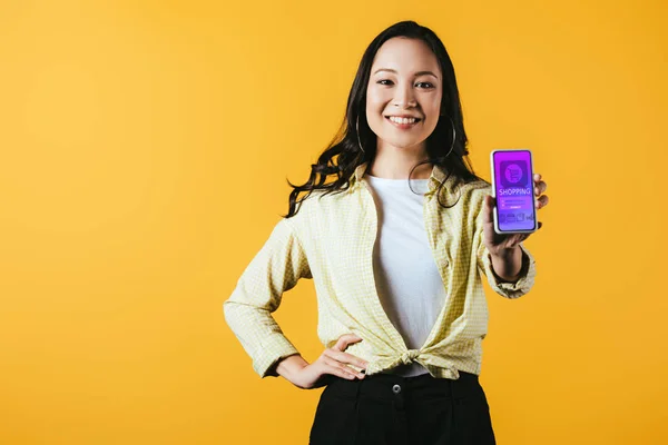 Menina asiática feliz mostrando smartphone com aplicativo de compras, isolado no amarelo — Stock Photo