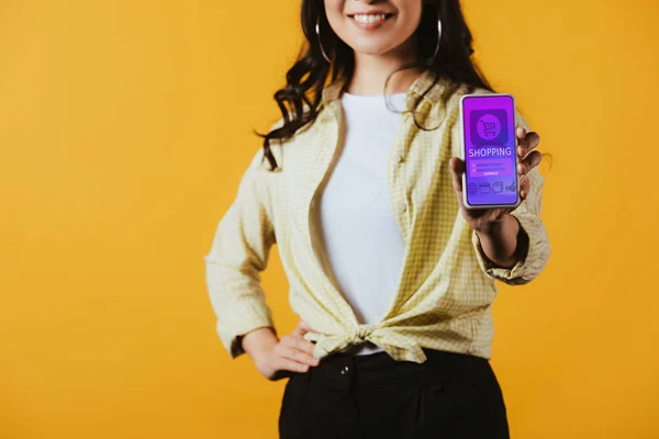 Vista recortada de chica morena mostrando teléfono inteligente con aplicación de compras, aislado en amarillo - foto de stock