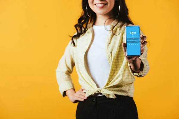 KYIV, UKRAINE - Abril 16, 2019: visão recortada de menina morena mostrando smartphone com aplicativo skype, isolado no amarelo — Fotografia de Stock