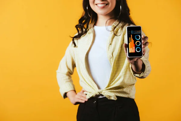 Cropped view of brunette girl showing smartphone with infographic, isolated on yellow — Stock Photo