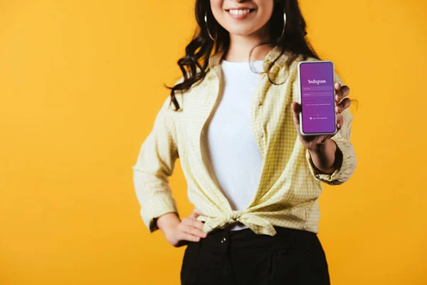 KYIV, UCRANIA - 16 DE ABRIL DE 2019: vista recortada de chica morena mostrando teléfono inteligente con aplicación instagram, aislado en amarillo - foto de stock