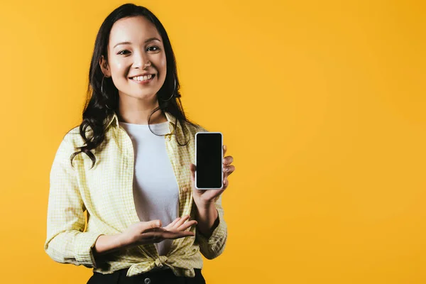 Приваблива азіатська дівчина, що представляє смартфон з порожнім екраном ізольовано на жовтому — стокове фото