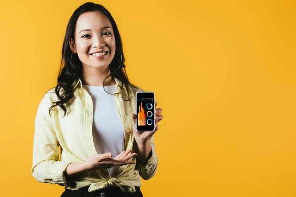 Chica asiática feliz presentando smartphone con infografía, aislado en amarillo - foto de stock