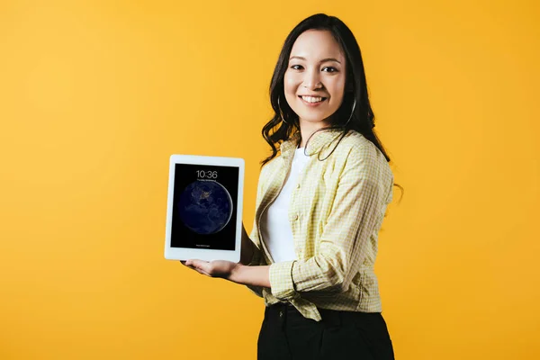 KYIV, UCRANIA - 16 DE ABRIL DE 2019: hermosa chica asiática mostrando la pantalla digital de la tableta, aislada en amarillo - foto de stock