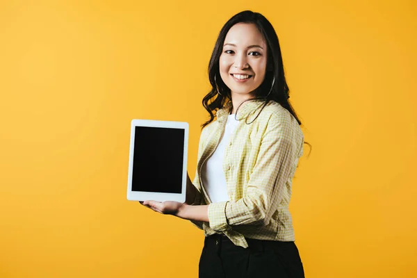 Lächelnde Asiatin zeigt digitales Tablet mit leerem Bildschirm, isoliert auf gelb — Stockfoto