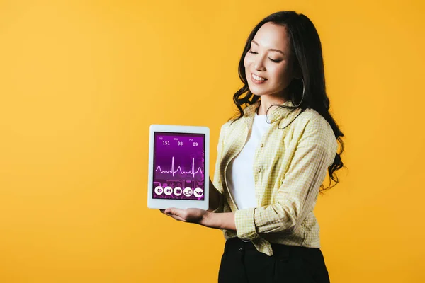 Felice ragazza asiatica mostrando tablet digitale con app salute, isolato su giallo — Foto stock
