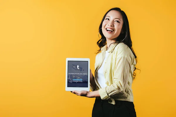 KYIV, UKRAINE - 16 de abril de 2019: menina asiática sorridente mostrando tablet digital com aplicativo tumblr, isolado em amarelo — Fotografia de Stock