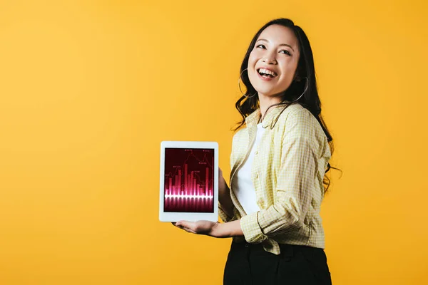 Улыбающаяся азиатская девушка показывает цифровой планшет с графиком, изолированный на желтом — стоковое фото
