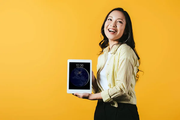 KYIV, UCRANIA - 16 DE ABRIL DE 2019: chica asiática sonriente mostrando la pantalla de la tableta digital, aislada en amarillo - foto de stock