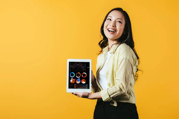 Улыбающаяся азиатская девушка показывает цифровой планшет с инфографическим приложением, изолированным на желтом — стоковое фото