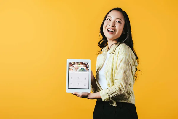 KYIV, UCRAINA - 16 APRILE 2019: bellissima ragazza asiatica che mostra tablet digitale con app quadrata, isolata su giallo — Foto stock