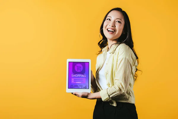 Sonriendo chica asiática mostrando tableta digital con aplicación de compras, aislado en amarillo - foto de stock