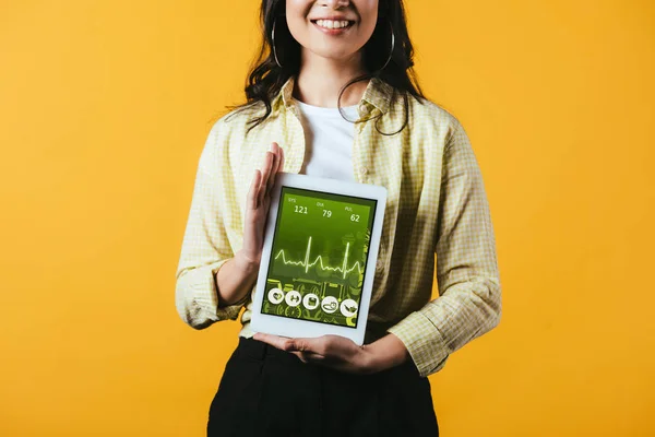 Recortado vista de chica sonriente mostrando tableta digital con aplicación de salud, aislado en amarillo - foto de stock