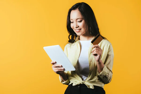 Привлекательная азиатская девушка покупки онлайн с цифровым планшетом и кредитной карты, изолированные на желтый — стоковое фото