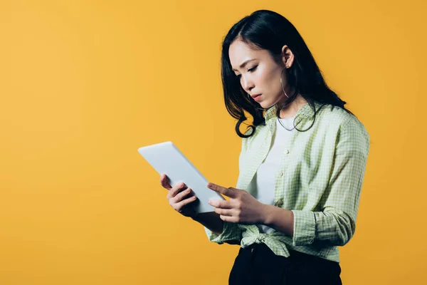 Disgustada chica asiática utilizando tableta digital, aislado en amarillo - foto de stock