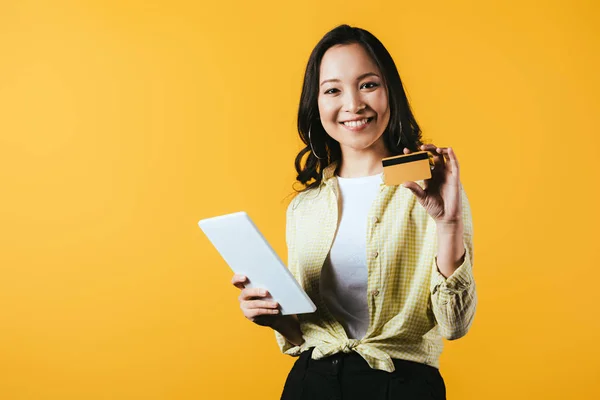 Lächelnde Asiatin beim Online-Shopping mit digitalem Tablet und Kreditkarte, isoliert auf gelb — Stockfoto