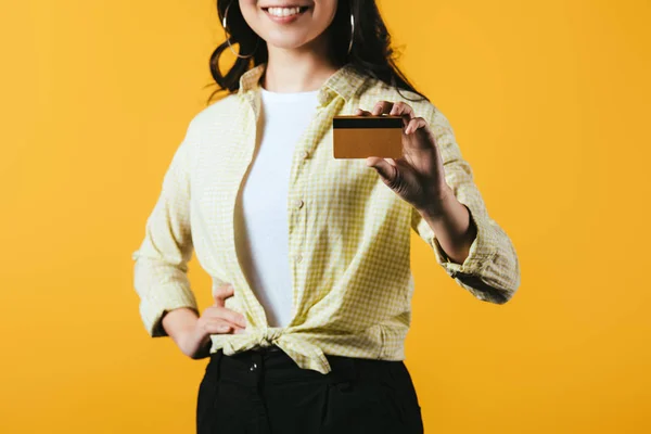 Обрезанный вид улыбающейся женщины, держащей кредитную карту, изолированную на желтый — стоковое фото