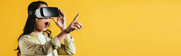 Excited girl pointing and using Virtual reality headset, isolated on yellow — Stock Photo