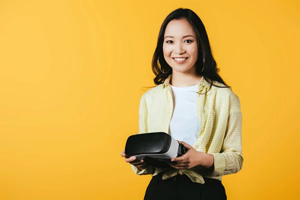 Smiling asian girl holding Virtual reality headset, isolated on yellow — Stock Photo