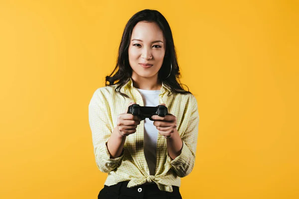 KYIV, UKRAINE - 16 de abril de 2019: mulher asiática sorridente jogando videogame com joystick, isolada em amarelo — Fotografia de Stock