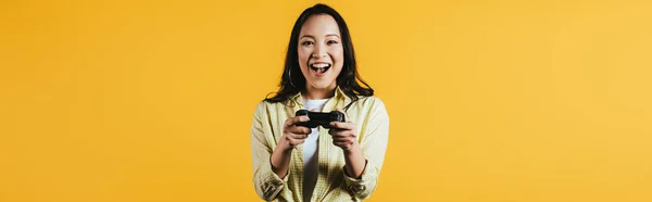 KYIV, UKRAINE - 16 avril 2019 : femme asiatique heureuse jouant à un jeu vidéo avec joystick, isolée sur jaune — Photo de stock